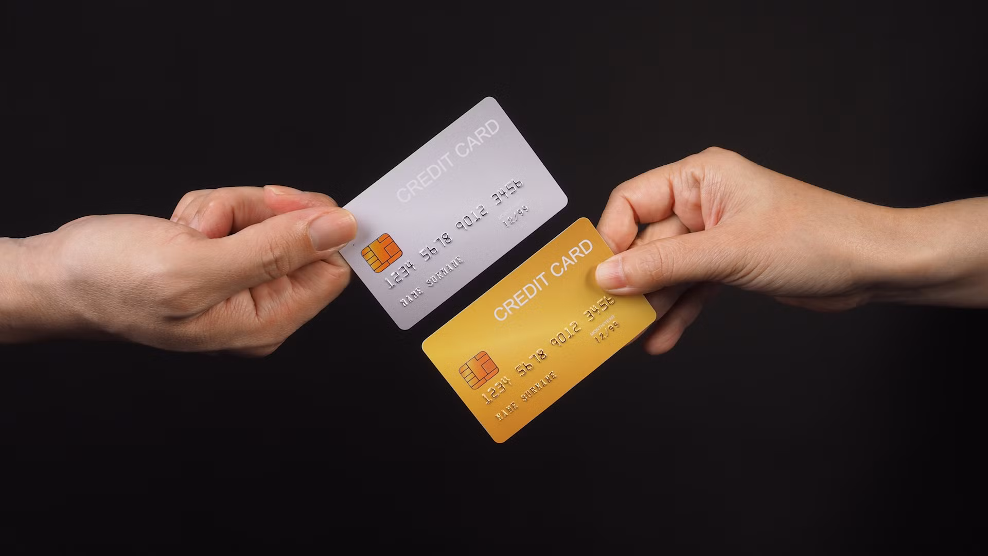 Two hands holding credit cards with black background