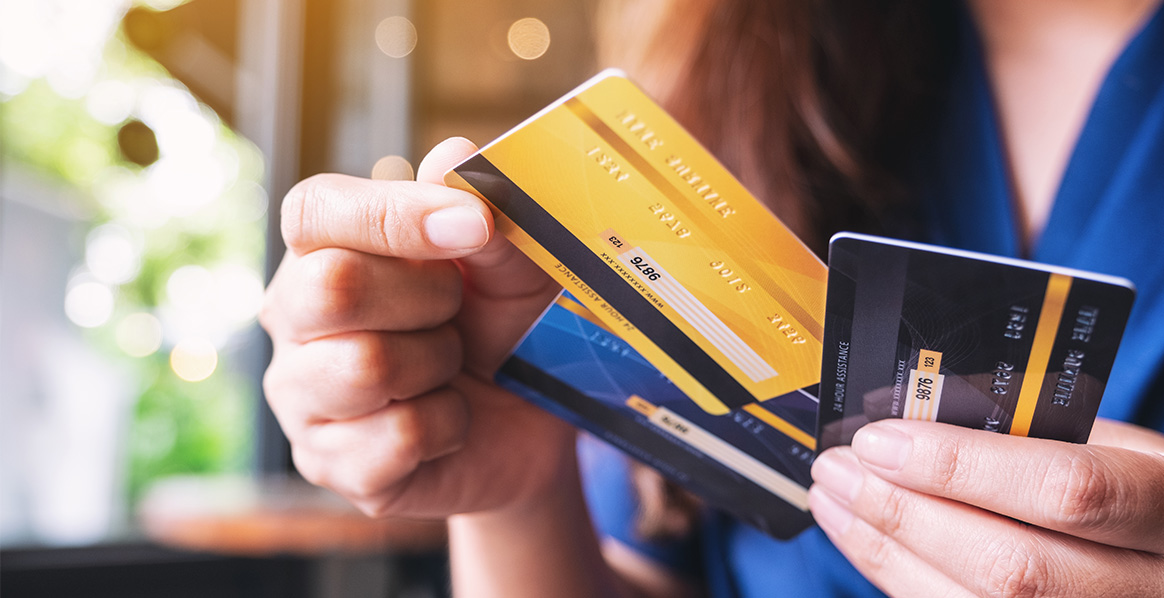 A person holding three credit or debit cards, showing the gold, black, and blue colors
